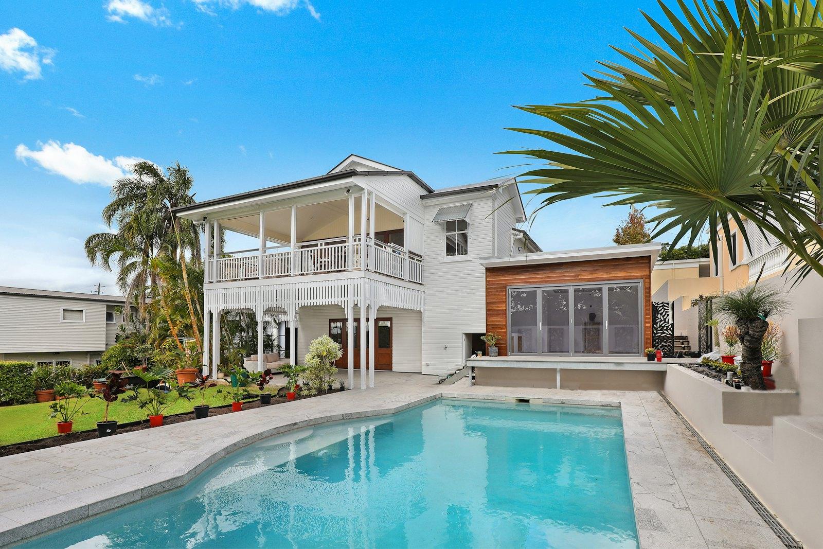 A white two-story home with palms and a pool under a Southern California sky